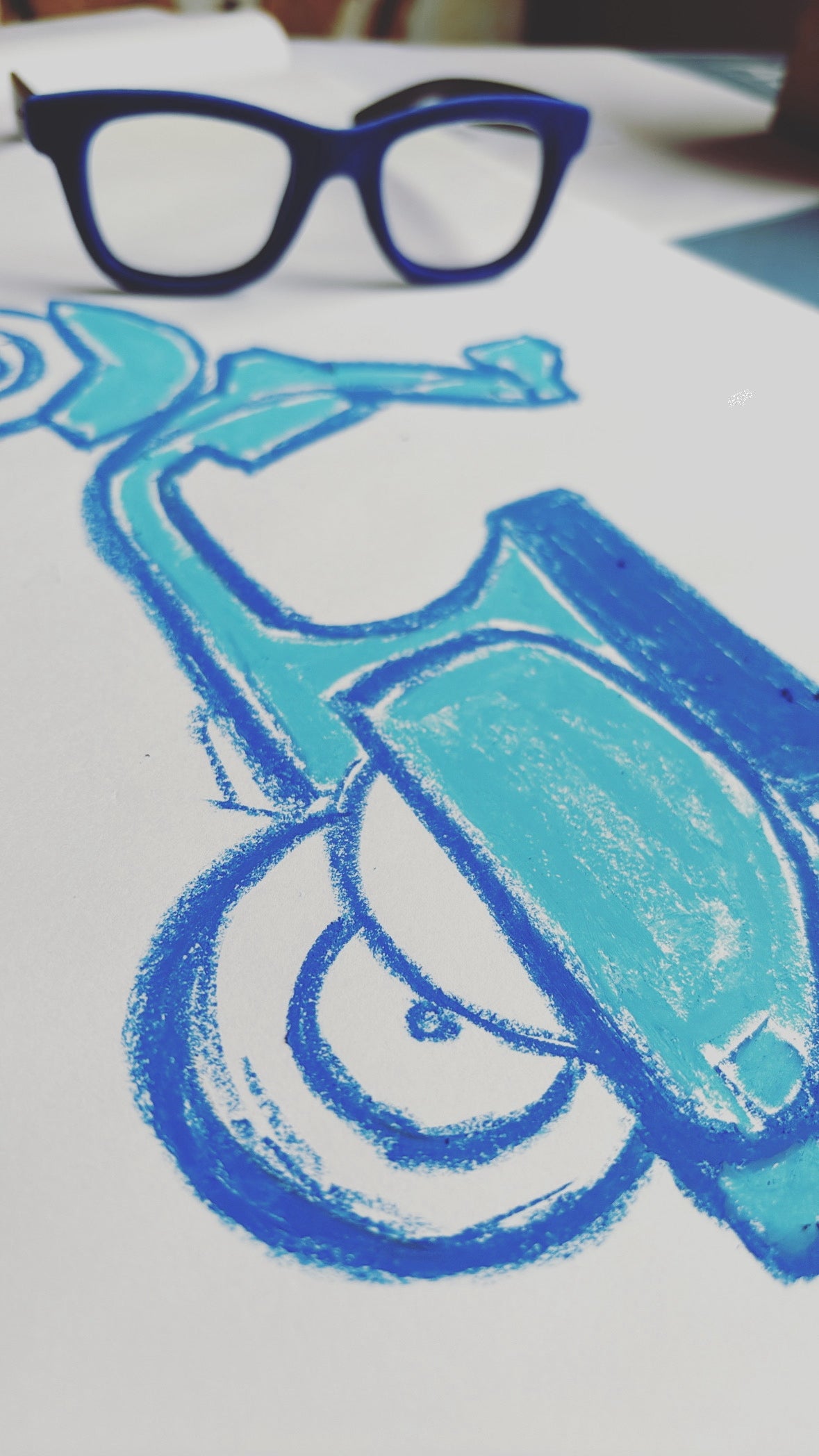 A close-up of a blue and turquoise chalk or pastel drawing of a vespa scooter on white paper, with a pair of blue velvet eyeglasses resting at the top of the frame.